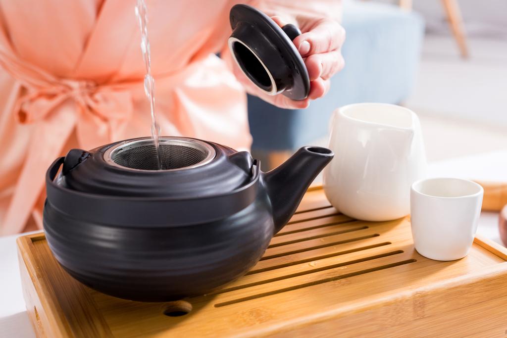 обрезанный снимок женщины, заваривающей чай во время чайной церемонии утром дома
 - Фото, изображение
