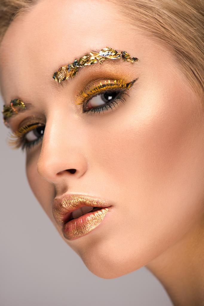 headshot de mulher atraente com maquiagem dourada brilhante olhando para a câmera isolada em cinza
 - Foto, Imagem