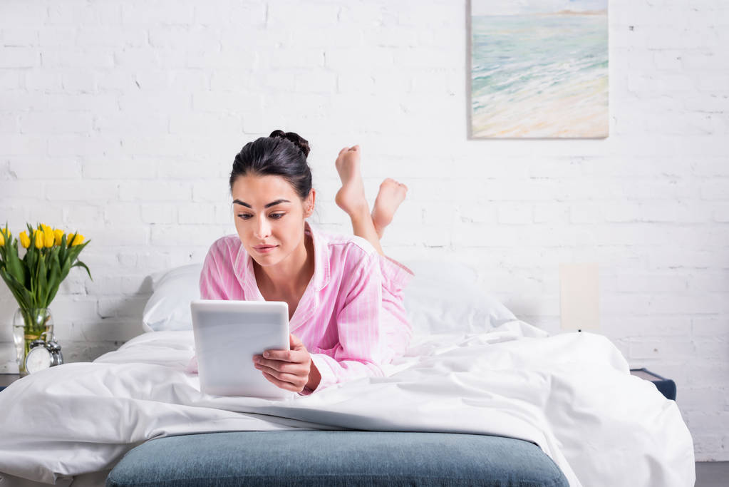 Žena v pyžamu pomocí tabletu vleže na posteli doma - Fotografie, Obrázek