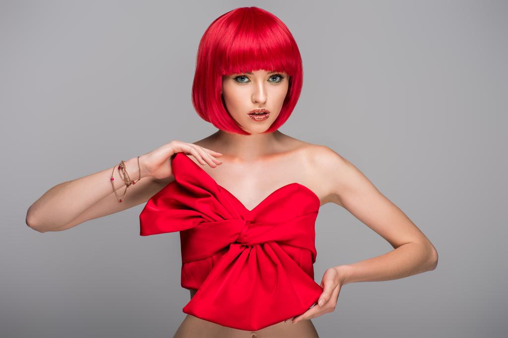 ελκυστική γυναίκα με κόκκινα μαλλιά και κόκκινο top βλέπουν φωτογραφική μηχανή που απομονώνονται σε γκρι - Φωτογραφία, εικόνα
