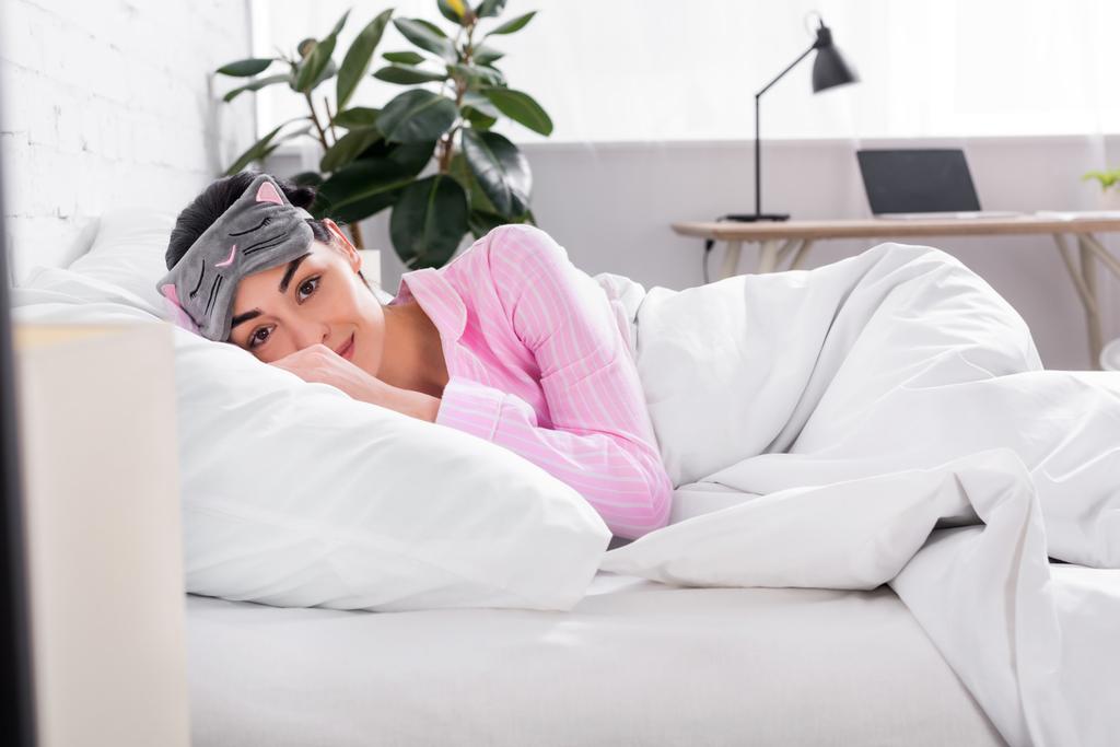 portrait of woman in pink pajamas and sleeping mask lying in bed at home - Photo, Image