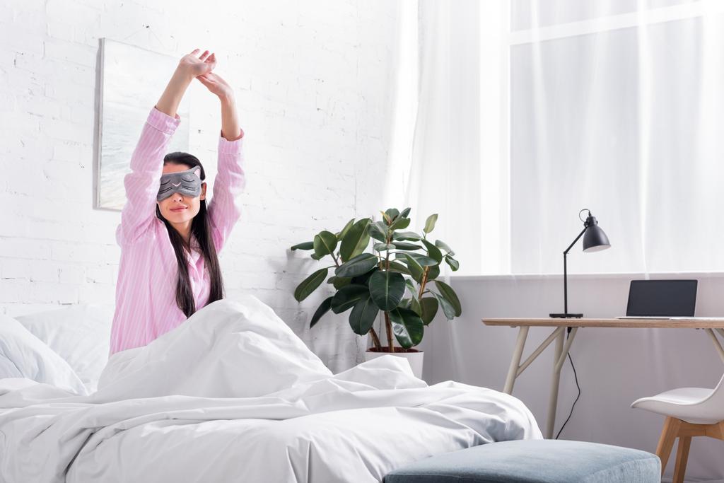 Πορτρέτο γυναίκας σε ροζ πιτζάμες και μάσκα ύπνου που εκτείνεται στο κρεβάτι το πρωί - Φωτογραφία, εικόνα