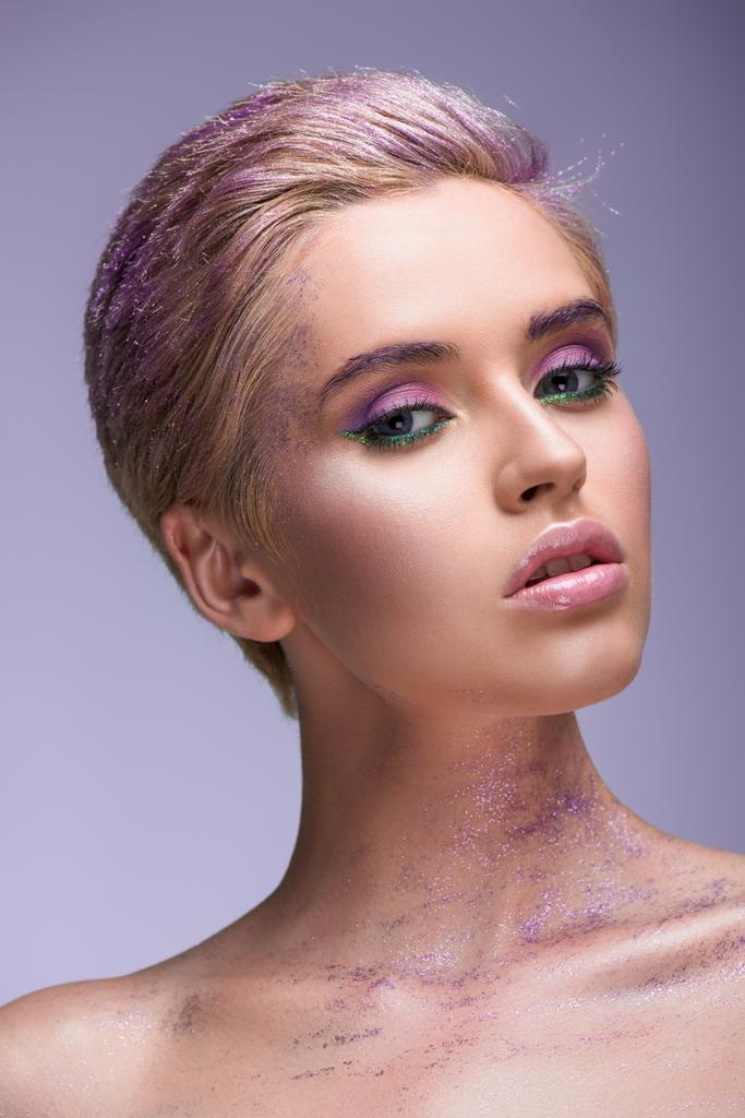 attractive woman with violet glitter on neck and short hair looking at camera isolated on violet - Photo, Image