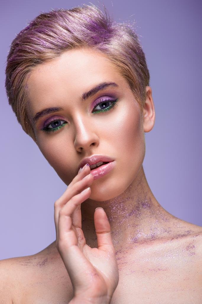 attractive woman with violet glitter on neck and short hair touching lips isolated on violet - Photo, Image