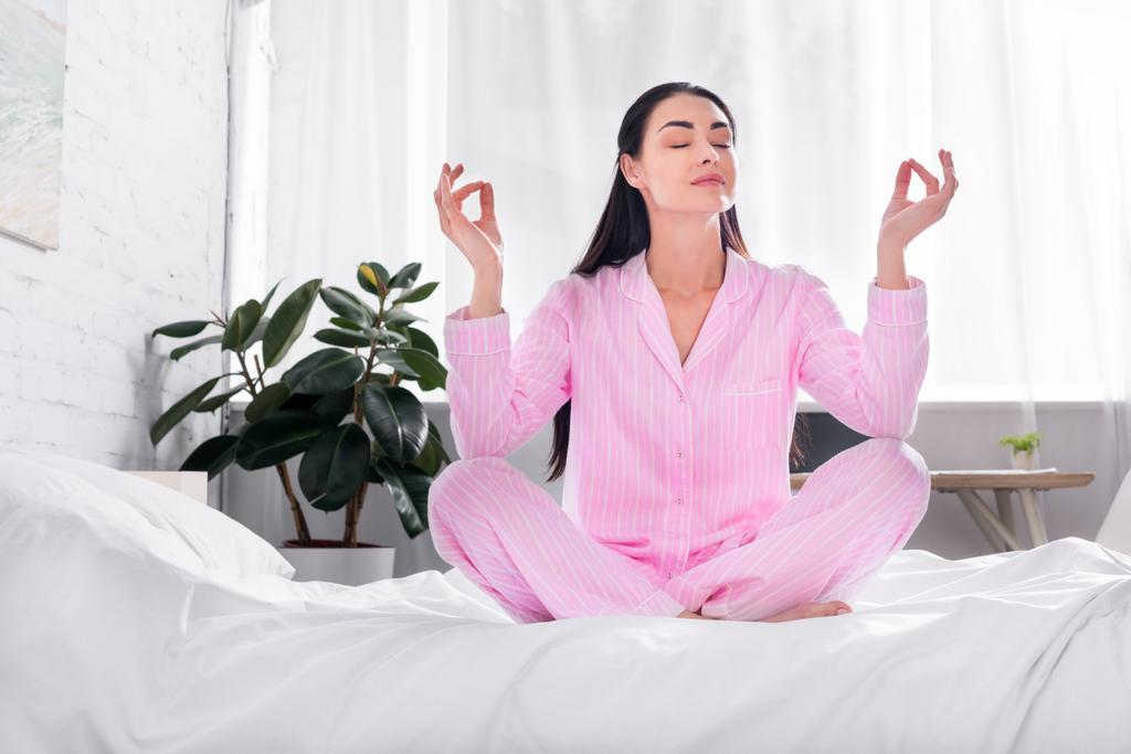 mujer en pijama rosa sentada en pose de loto en la cama por la mañana en casa
 - Foto, Imagen