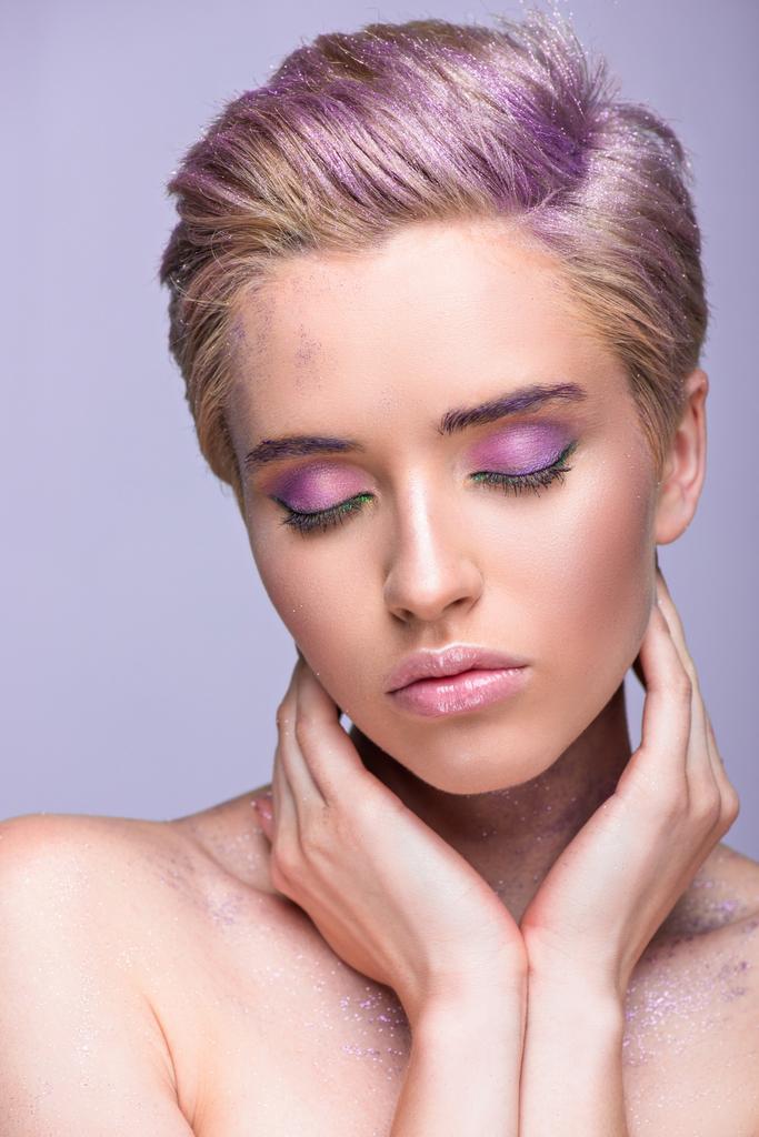 atractiva mujer con brillo violeta en el cuello y pelo corto tocando el cuello con los ojos cerrados aislados en violeta
 - Foto, Imagen
