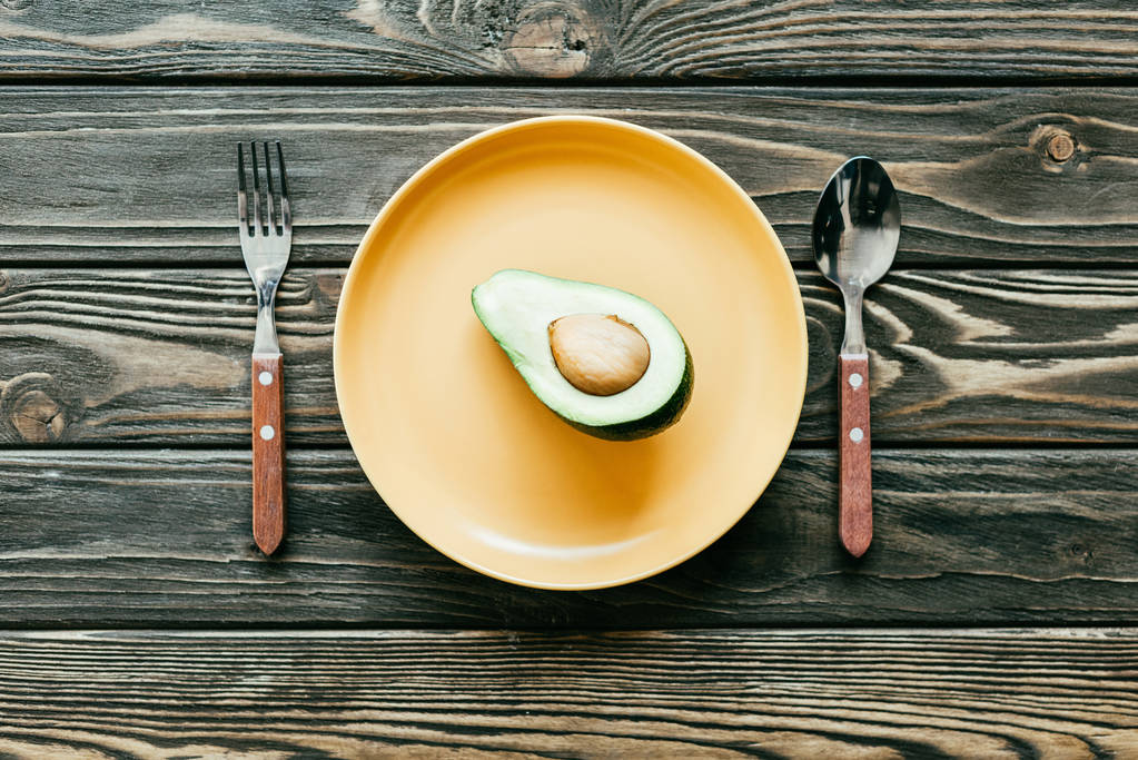 Avocado auf Teller mit Löffel und Gabel auf Holztisch serviert - Foto, Bild