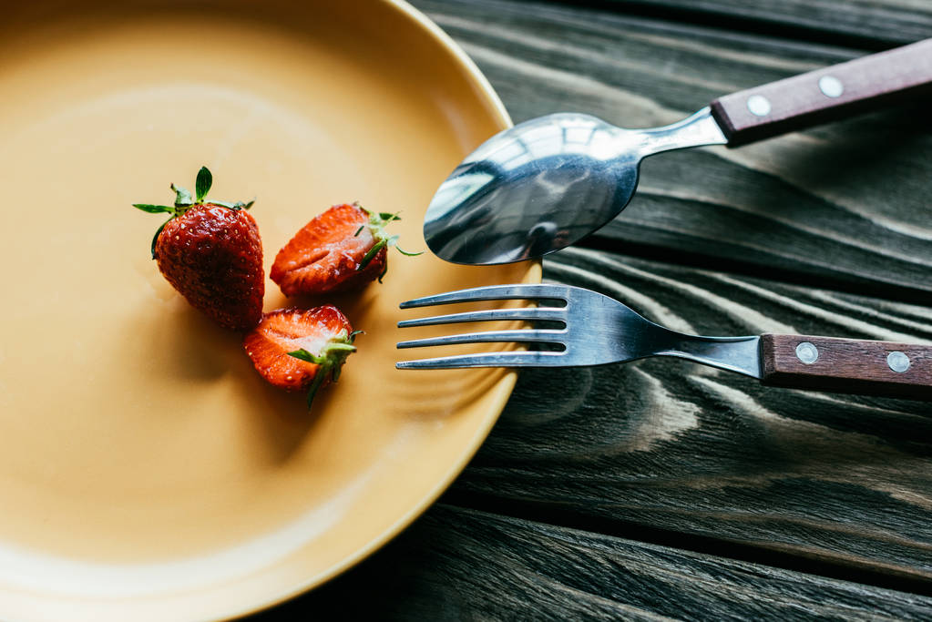 Gabel und Löffel auf Teller mit Erdbeeren auf Holztisch - Foto, Bild
