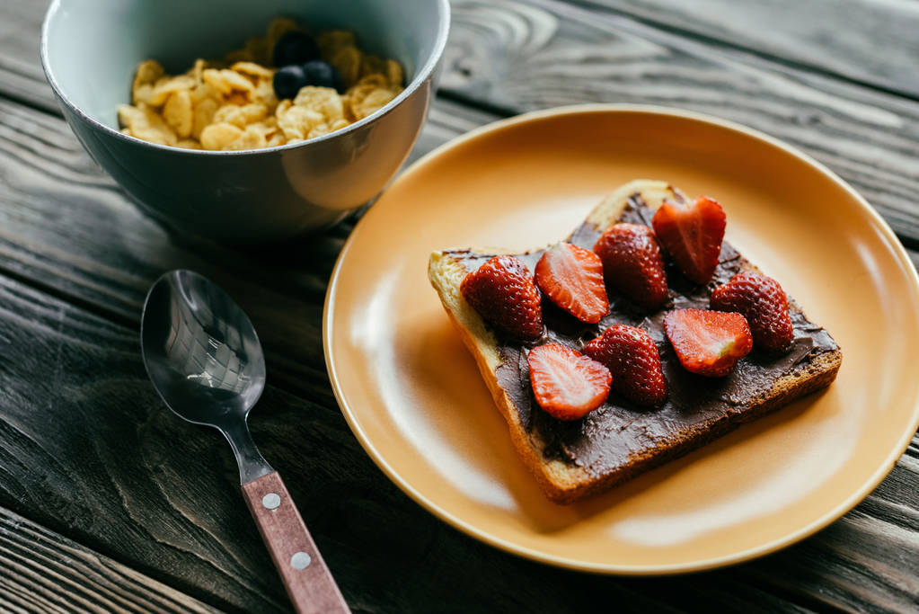 Desayuno con hojuelas de maíz y tostadas con fresas en mesa de madera
 - Foto, imagen