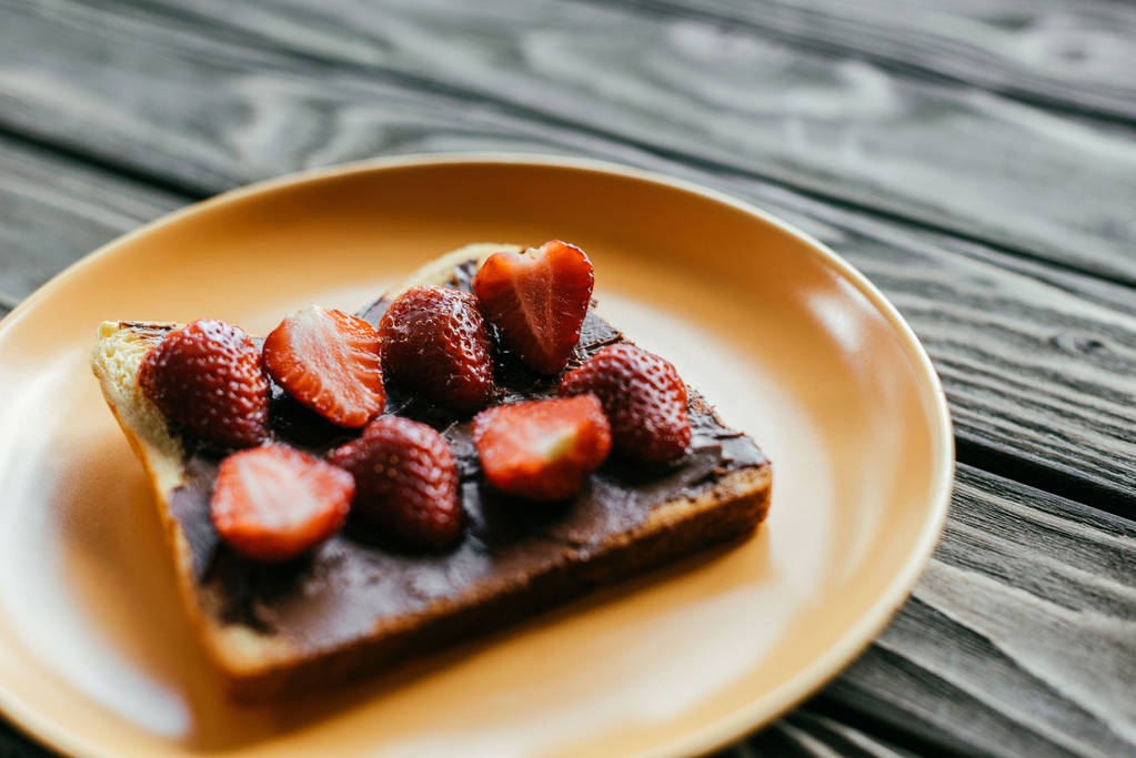 Brot mit Schokoladenaufstrich und Erdbeeren auf Holztisch - Foto, Bild