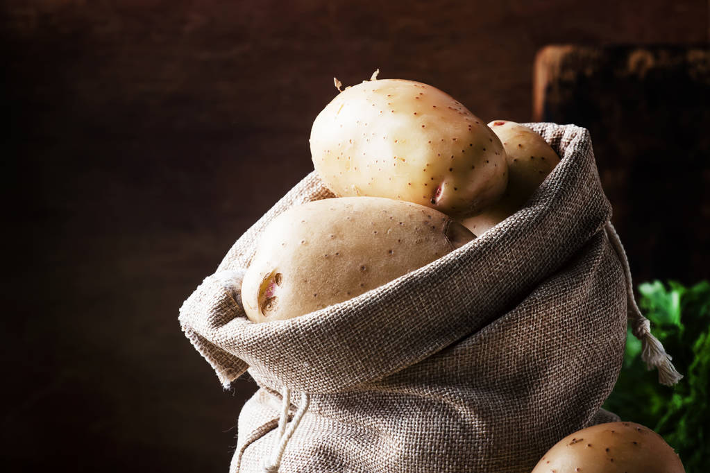 Verse rauwe aardappelen in een doek zak, houten achtergrond, rustieke stijl, selectieve aandacht - Foto, afbeelding