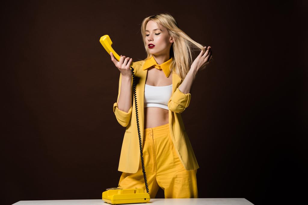 όμορφη νεαρή ξανθιά γυναίκα με κίτρινα ρούχα μιλάει με περιστροφικό τηλέφωνο για καφέ  - Φωτογραφία, εικόνα