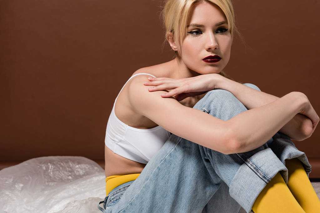 nachdenkliche junge blonde Frau sitzt und schaut weg auf braun  - Foto, Bild