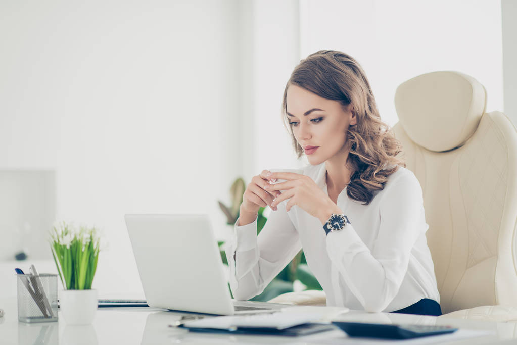 Modaya uygun, şık, çekici, güzel, güzel kadın iş yerinde merkezinde oturan elinde çay bir fincan sahip film video izlerken laptop, ekrana bakarak beyaz gömlekli modern saç modeli ile portresi - Fotoğraf, Görsel