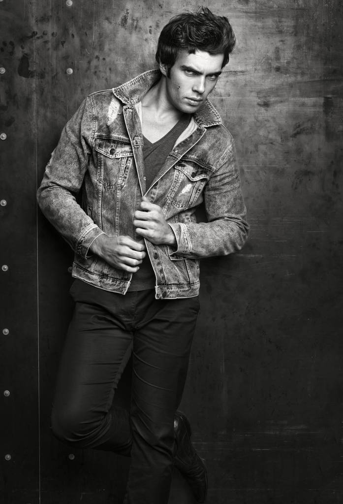 Men's fashion portrait. Young handsome man posing in denim jacket on a background of metal wall. A suspicious look at the person - Photo, Image
