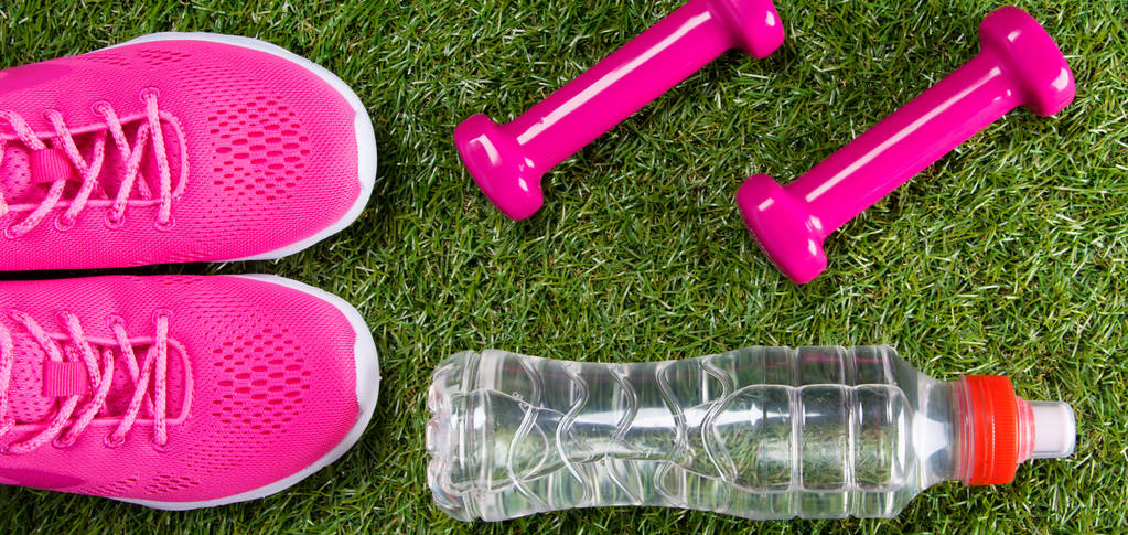 rosa Turnschuhe und Hanteln für Fitness, eine Flasche Wasser, vor dem Hintergrund von Gras - Foto, Bild