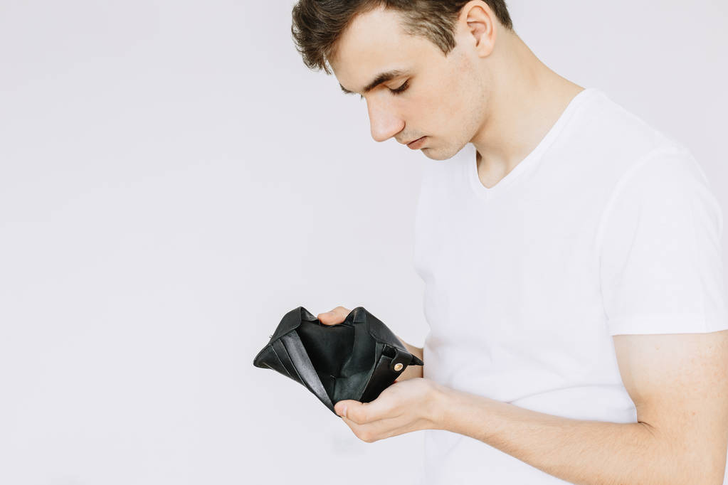 Ein junger Mann blickt in eine leere Brieftasche. isolierter weißer Hintergrund - Foto, Bild