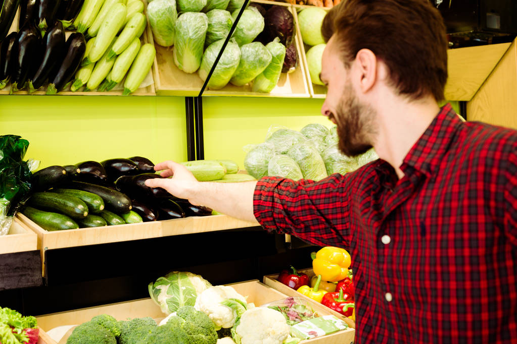 Caucásico hombre en rojo camisa a cuadros la elección de verduras en el supermercado
 - Foto, Imagen