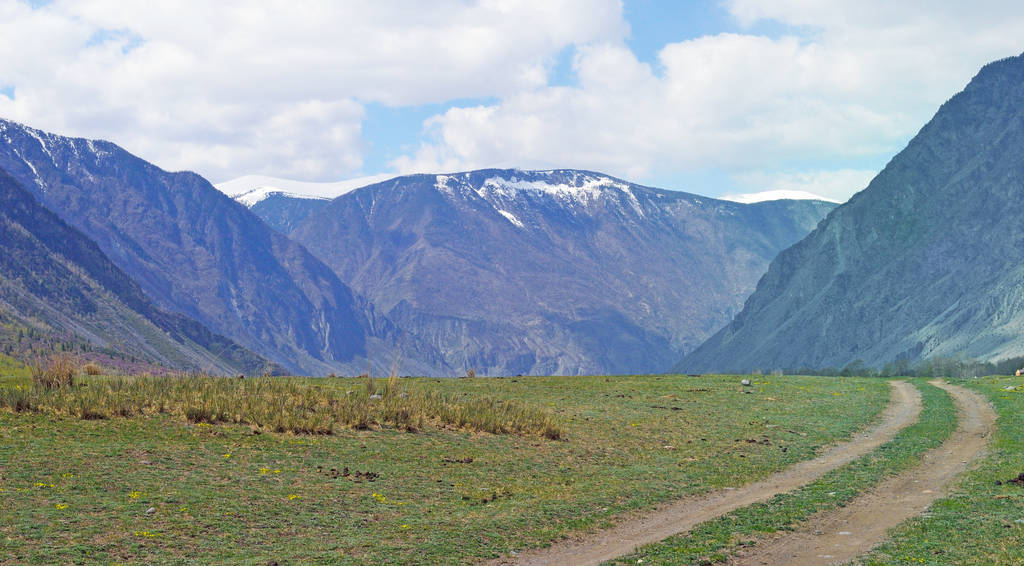 ένας χωματόδρομος τοποθετούνται κατά μήκος μιας ορεινής κοιλάδας ανάμεσα στα βουνά - Φωτογραφία, εικόνα