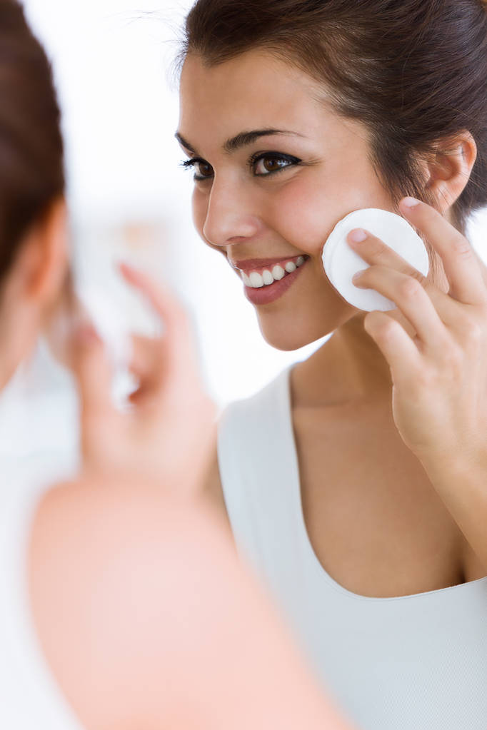 Schot van mooie jonge vrouw is het reinigen van haar gezicht terwijl het zoeken in de spiegel in de badkamer. - Foto, afbeelding
