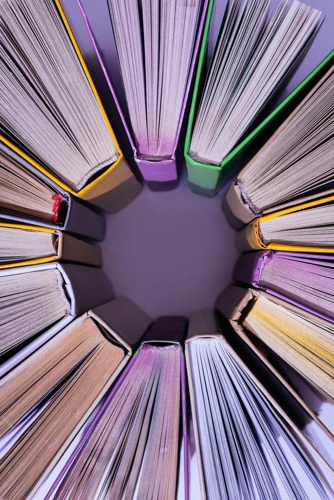 pohled shora zásobníku barevných knih v kruhu na fialové stůl - Fotografie, Obrázek