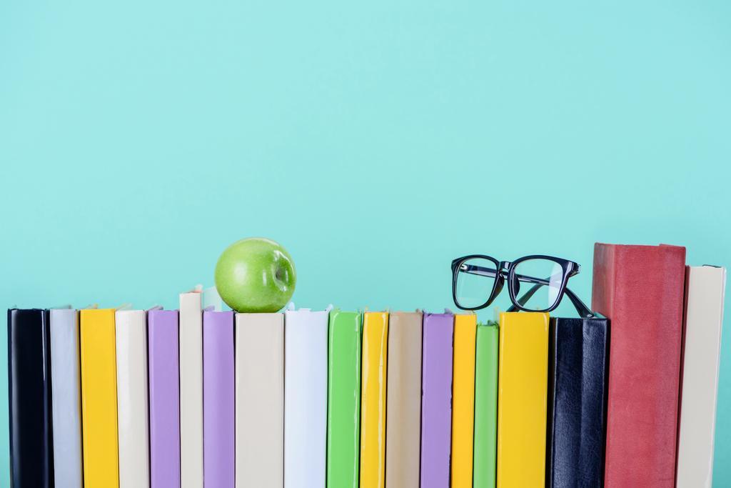 rij van boeken met appel en glazen geïsoleerd op blauw - Foto, afbeelding