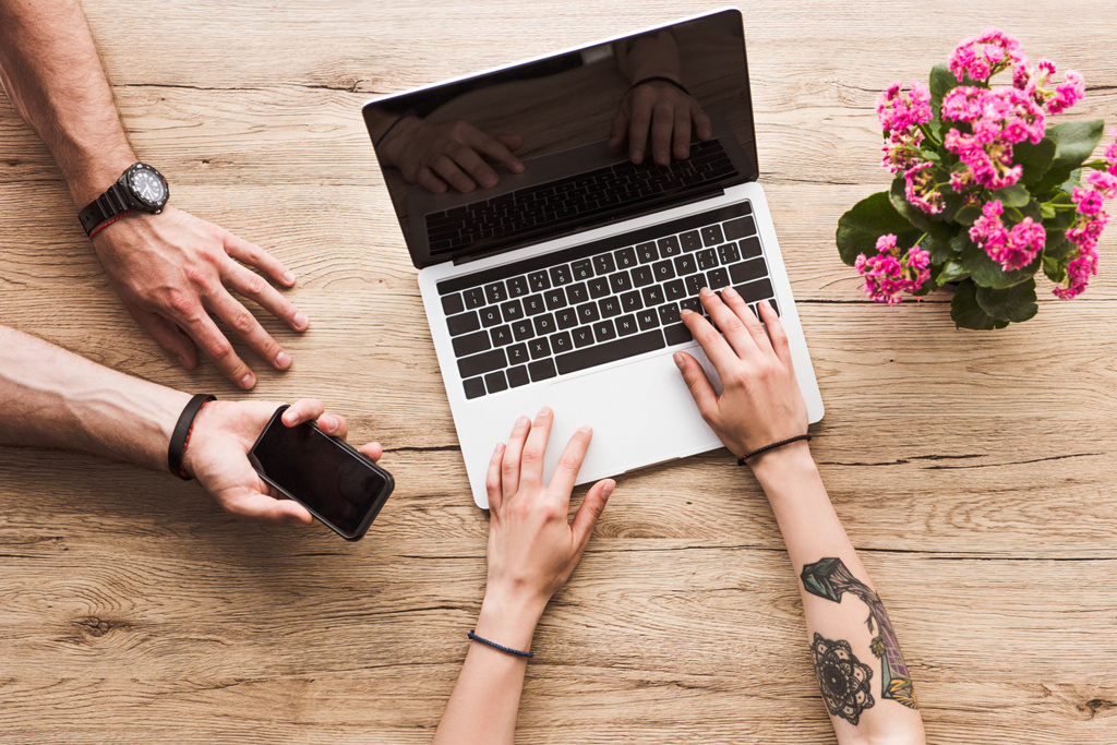 Schnappschuss von Mann mit Smartphone in der Hand und Frau am Tisch mit Laptop und Kalanchoe-Blume - Foto, Bild