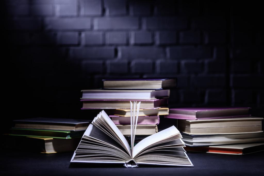Offenes Buch vor Bücherstapel auf dunkler Oberfläche - Foto, Bild