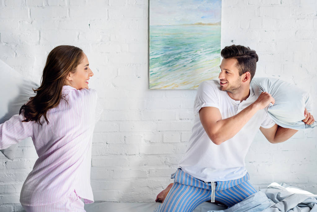 young happy girlfriend and boyfriend having pillow fight in bedroom  - Photo, Image