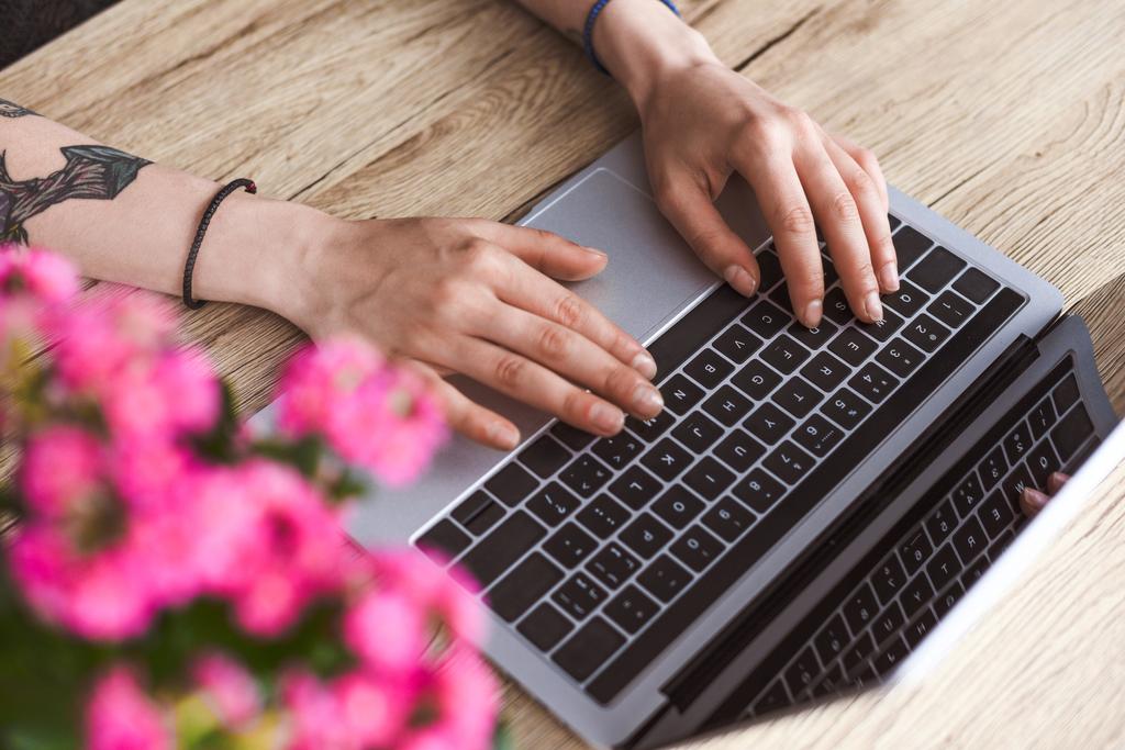 részleges kilátás nyílik a tetovált nő dolgozik laptop asztalhoz a virágok  - Fotó, kép