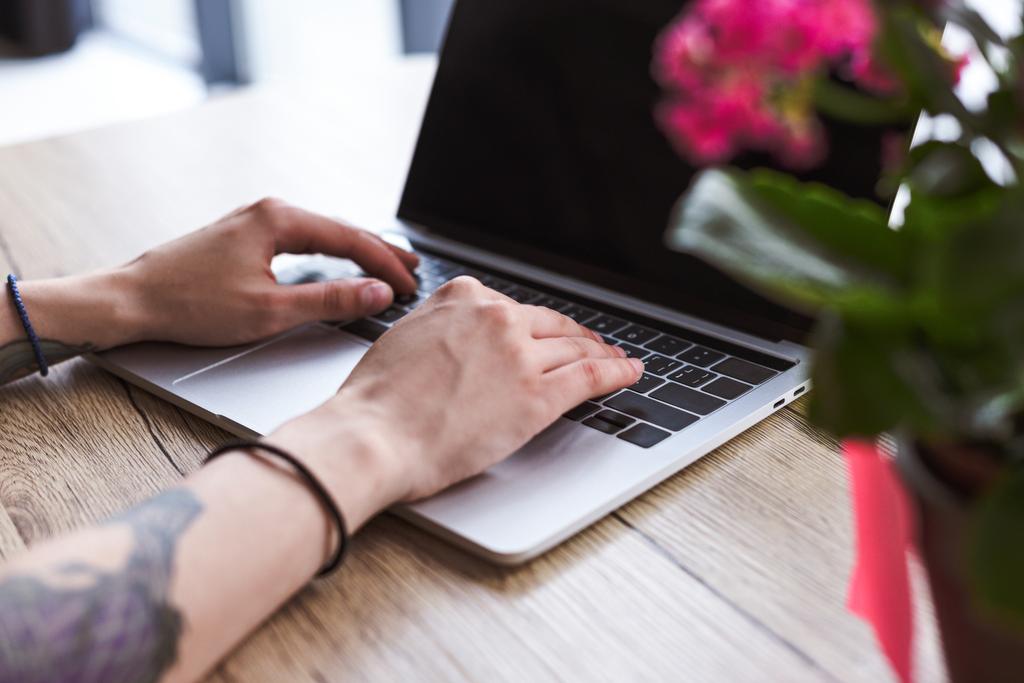 immagine ritagliata di donna con le mani tatuate digitando sul computer portatile a tavola con i fiori
  - Foto, immagini