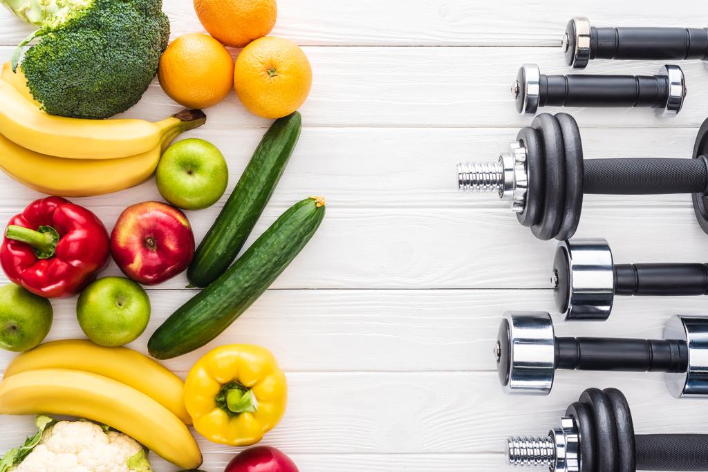 top view of fresh fruits with vegetables and various dumbbells on wooden surface - Photo, Image