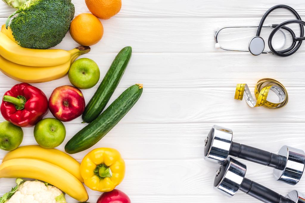 верхний вид свежих фруктов и овощей, гантели, стетоскоп и измерительная лента на деревянном столе
 - Фото, изображение