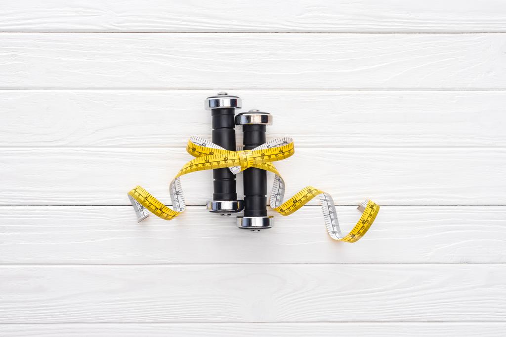 close-up view of dumbbells and yellow measuring tape on wooden surface - Photo, Image