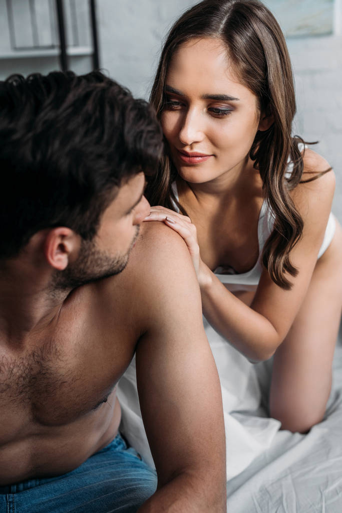 привлекательная девушка смотрит на парня, который трогает его плечо на кровати утром
 - Фото, изображение