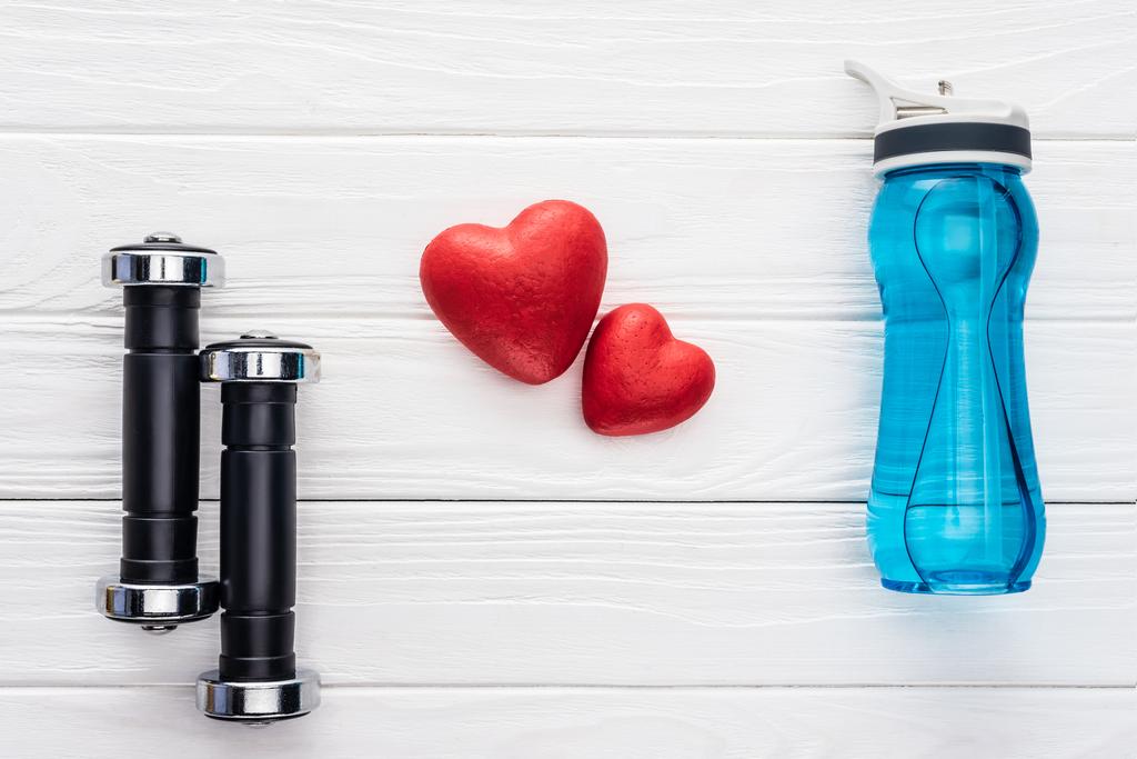 Draufsicht auf Hanteln, Wasserflasche und rote Herzen auf Holzoberfläche - Foto, Bild