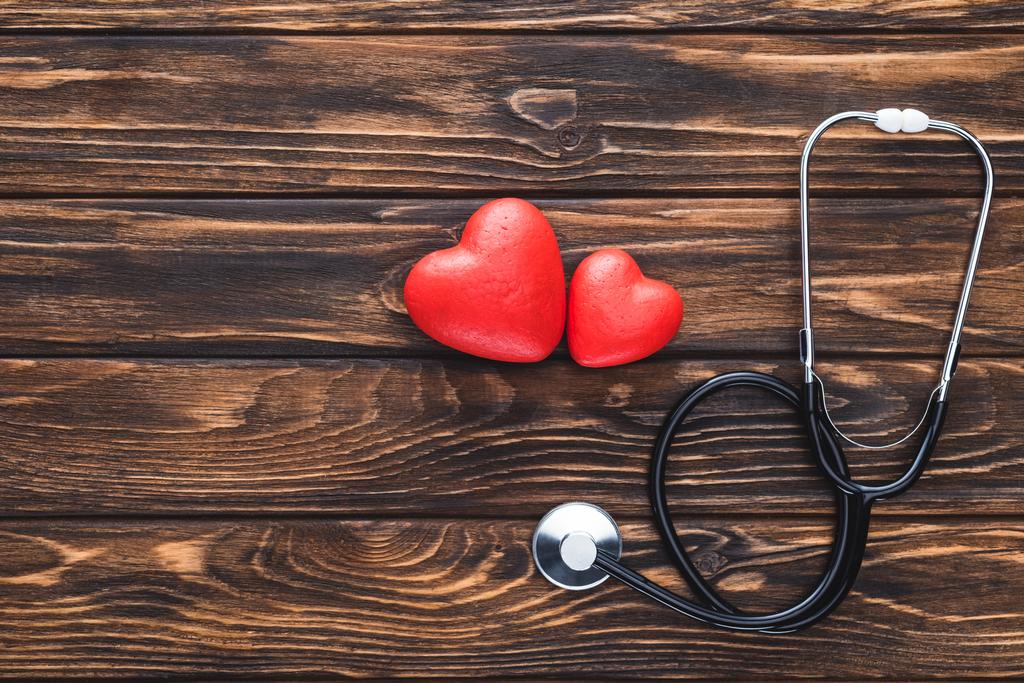 Draufsicht auf Stethoskop und rotes Herz-Symbol auf Holztischplatte   - Foto, Bild