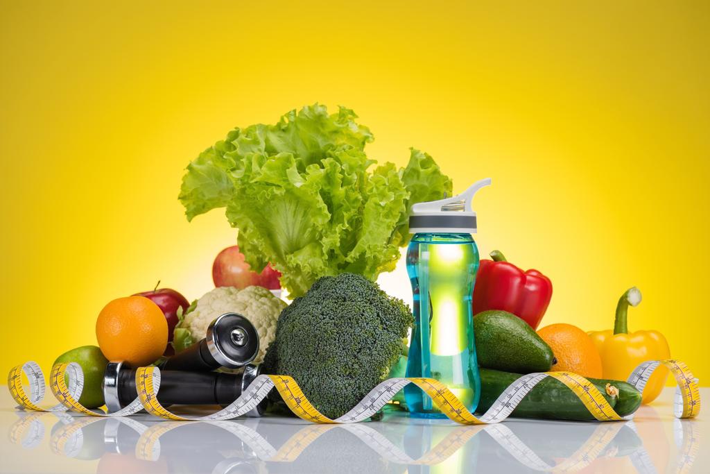 zbliżenie, świeżych owoców i warzyw, pomiaru taśmy, butelkę wody i hantle na żółty - Zdjęcie, obraz