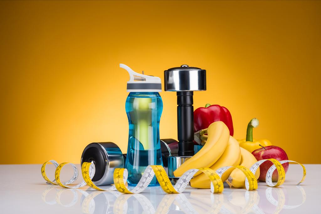 vista close-up de halteres, garrafa de água, fita métrica e pimentas com frutas em amarelo
 - Foto, Imagem