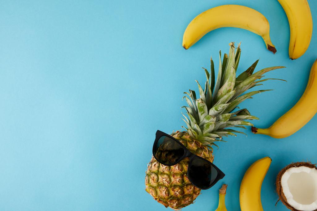 pohled shora čerstvý kokos, banány a ananas s izolované na modré sluneční brýle - Fotografie, Obrázek