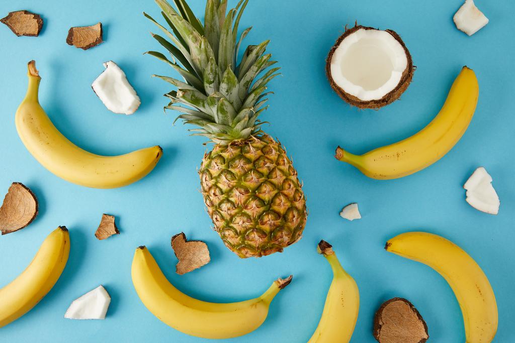 plat lag met verse ananas, bananen en kokosnoot stukken geïsoleerd op blauw - Foto, afbeelding