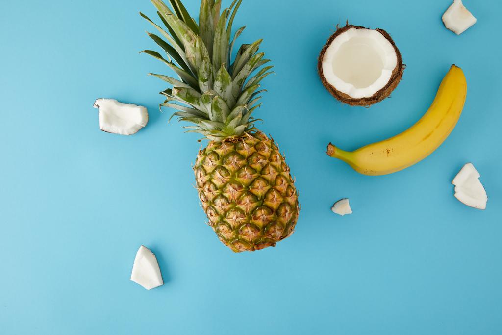 青に分離された熟したパイナップル、バナナ、ココナッツ部分とフラット レイアウト - 写真・画像