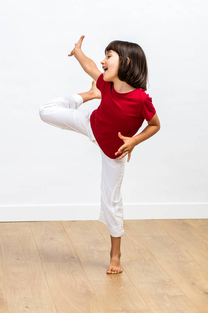 сміється динамічна 6-річна дитина насолоджується танцями та підняттям ніг та рук, щоб висловити радість, енергію та щастя над дерев'яною підлогою, білим тлом
 - Фото, зображення