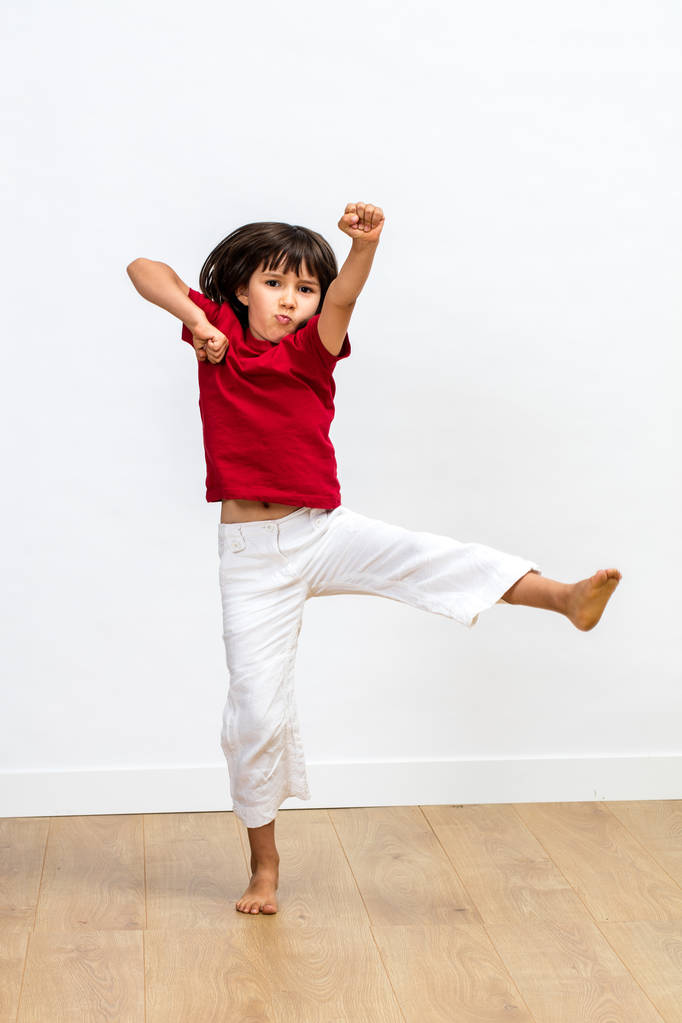 walki młodych dzieci z ramionami wywoływane, ciesząc się, wykonywanie sztuki walki, tai chi, kung fu lub taekwondo dla zabawy energiczny koncentracji i kid' sport na podłoże drewniane podłogi, biały - Zdjęcie, obraz