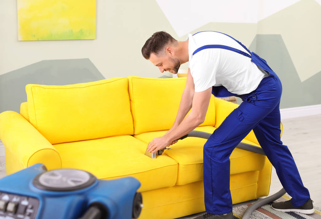 Працівник хімчистки видаляє бруд з дивана в приміщенні
 - Фото, зображення