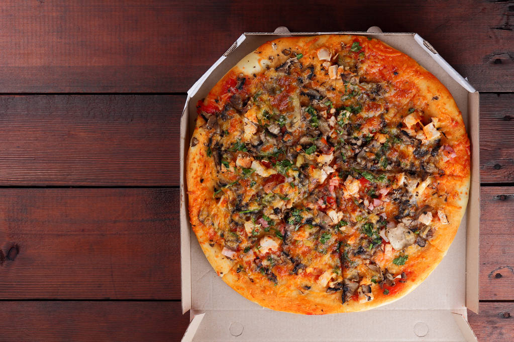 Pizza w polu na podłoże drewniane. Włoskiej pizzy z kurczaka, grzyby, zielenie, ser i sos. Świąteczny posiłek w tekturowym pudełku - Zdjęcie, obraz