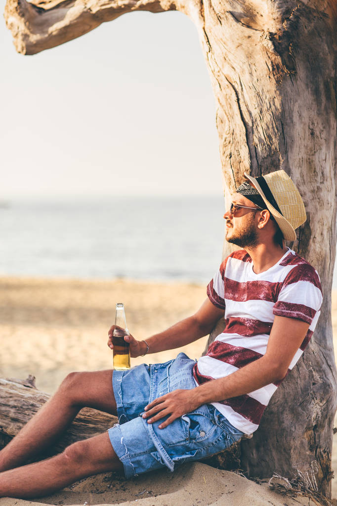 Joven sentado en la playa y bebiendo cerveza
 - Foto, Imagen