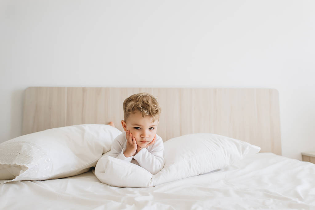 αξιολάτρευτο μικρό παιδί αγόρι στο λευκό κορμάκι ξαπλωμένος στο κρεβάτι στο σπίτι - Φωτογραφία, εικόνα