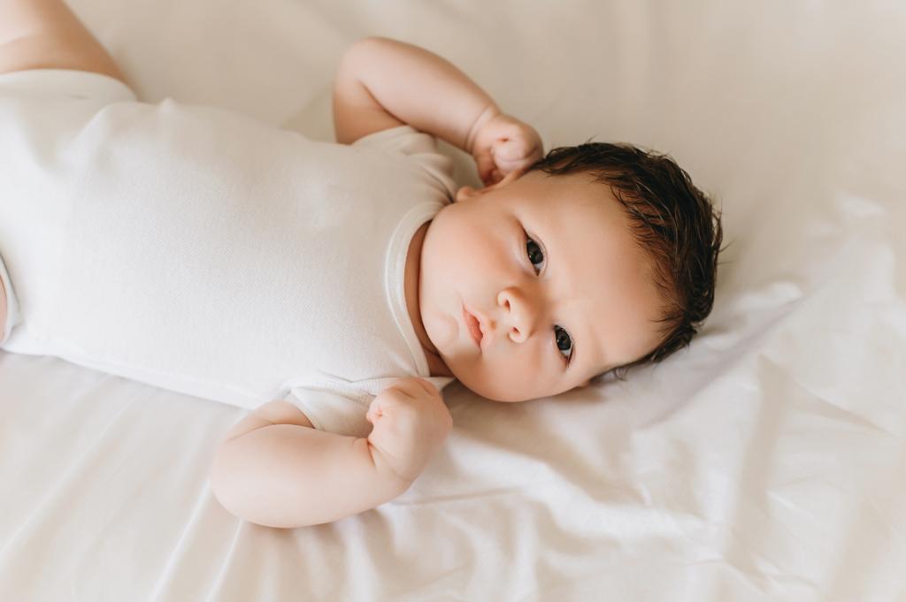 κλείνω πάνω θέα της χαριτωμένο νεογέννητο μωρό σε λευκό κορμάκι ξαπλωμένος στο κρεβάτι - Φωτογραφία, εικόνα