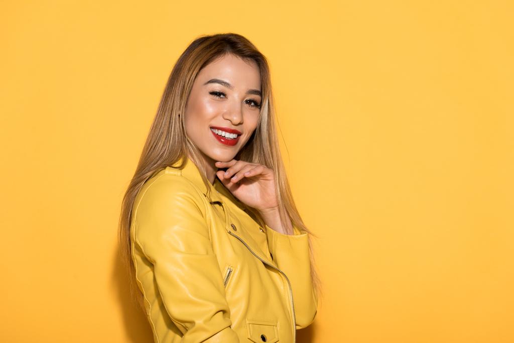 smiling asian stylish woman in leather jacket standing on yellow background  - Photo, Image
